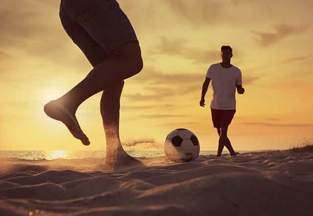 Football players on the beach at sunset