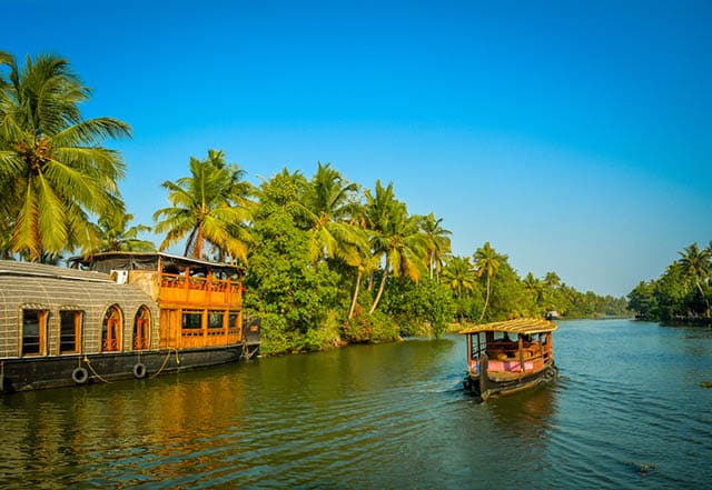 A tourist boat passes through a traditional Kerala houseboat on the backwater of Vembanad Lake, India